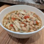 Chicken surrounded by white beans, onions, and garlic in a savory broth.